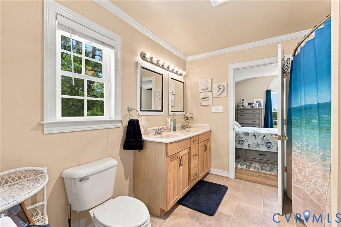 Neutral-toned bathroom featuring a dual vanity with light wood cabinetry and a laminate countertop