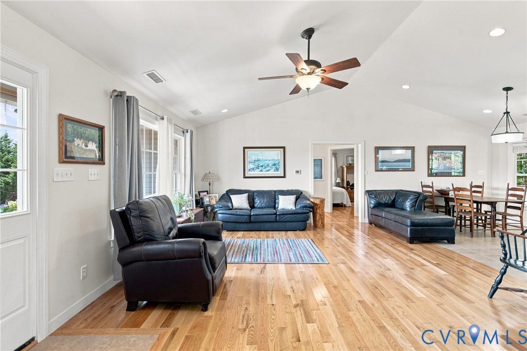 Vaulted ceilings define this expansive living area, featuring wood-finish flooring, recessed lighting, and a ceiling fan with integrated lighting
