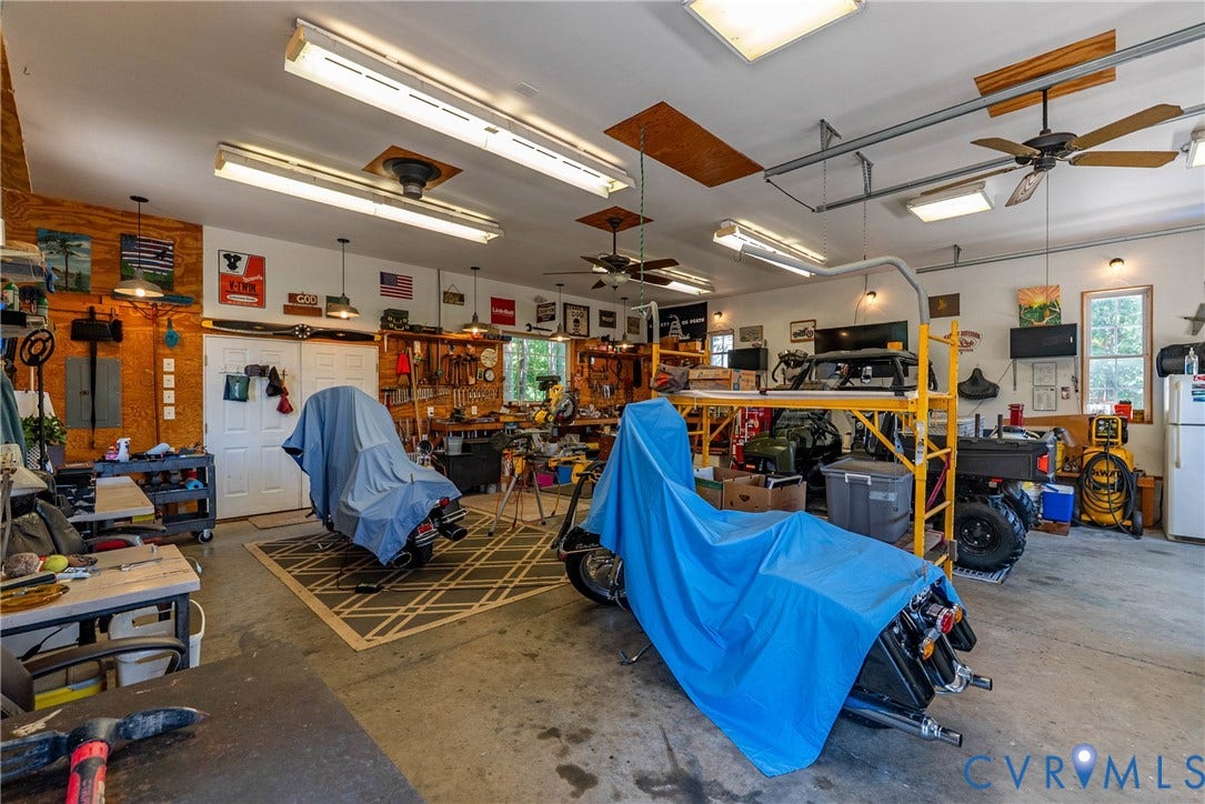 Spacious garage featuring concrete flooring, multiple ceiling fans, abundant overhead fluorescent lighting, and two windows providing natural light