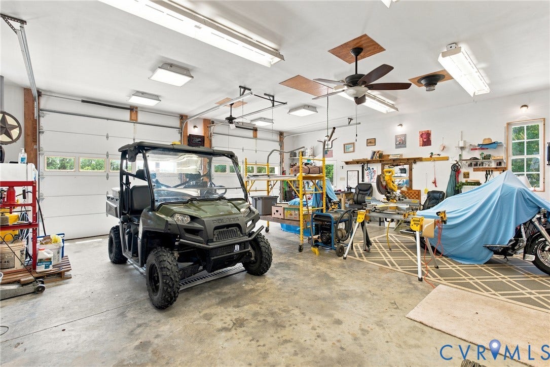 Spacious garage featuring two overhead doors with window panels, multiple ceiling fans, abundant overhead lighting, and concrete flooring