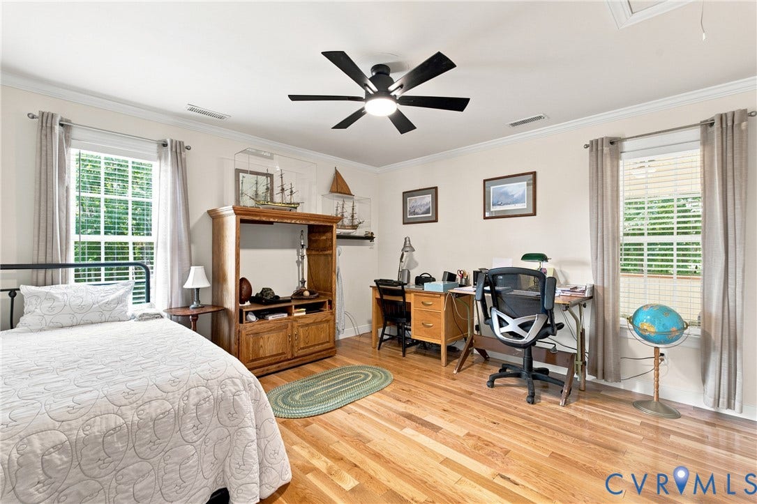 Hardwood-finish flooring throughout, featuring a ceiling fan with integrated lighting, crown molding, and two windows with blinds