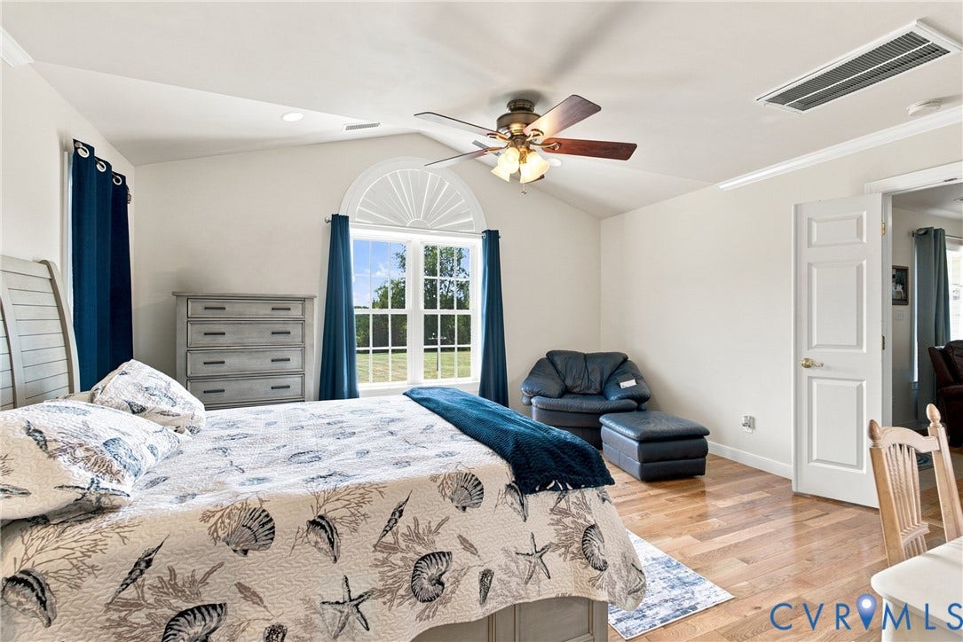 Vaulted ceiling bedroom with a large arched window, wood-finish flooring, and a ceiling fan with integrated lighting