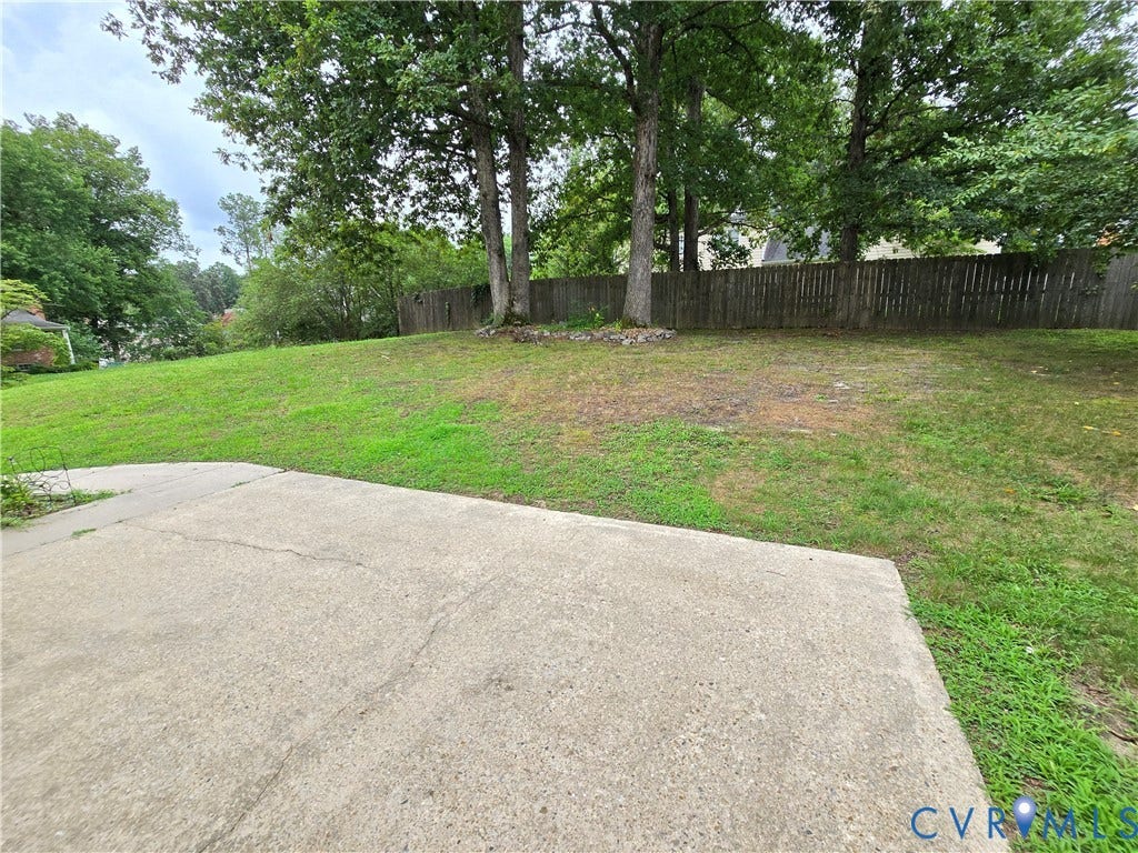 3901 Buckland Place, Chester, VA 23831 Spacious backyard featuring a concrete patio, sloped grassy lawn, mature trees, and a privacy fence