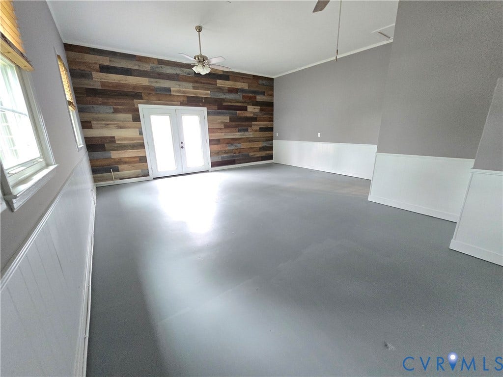 3901 Buckland Place, Chester, VA 23831 Spacious room featuring a multi-toned wood plank accent wall, concrete floor, and white French doors