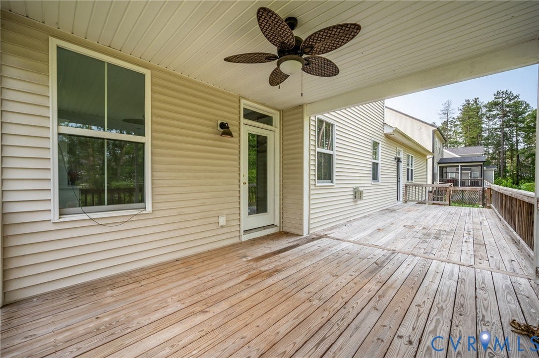 7130 Maple Summit Lane, Moseley, VA 23120 Expansive covered wood-finish deck with a ceiling fan, showcasing light-colored siding, multiple windows, and a glass-paneled door