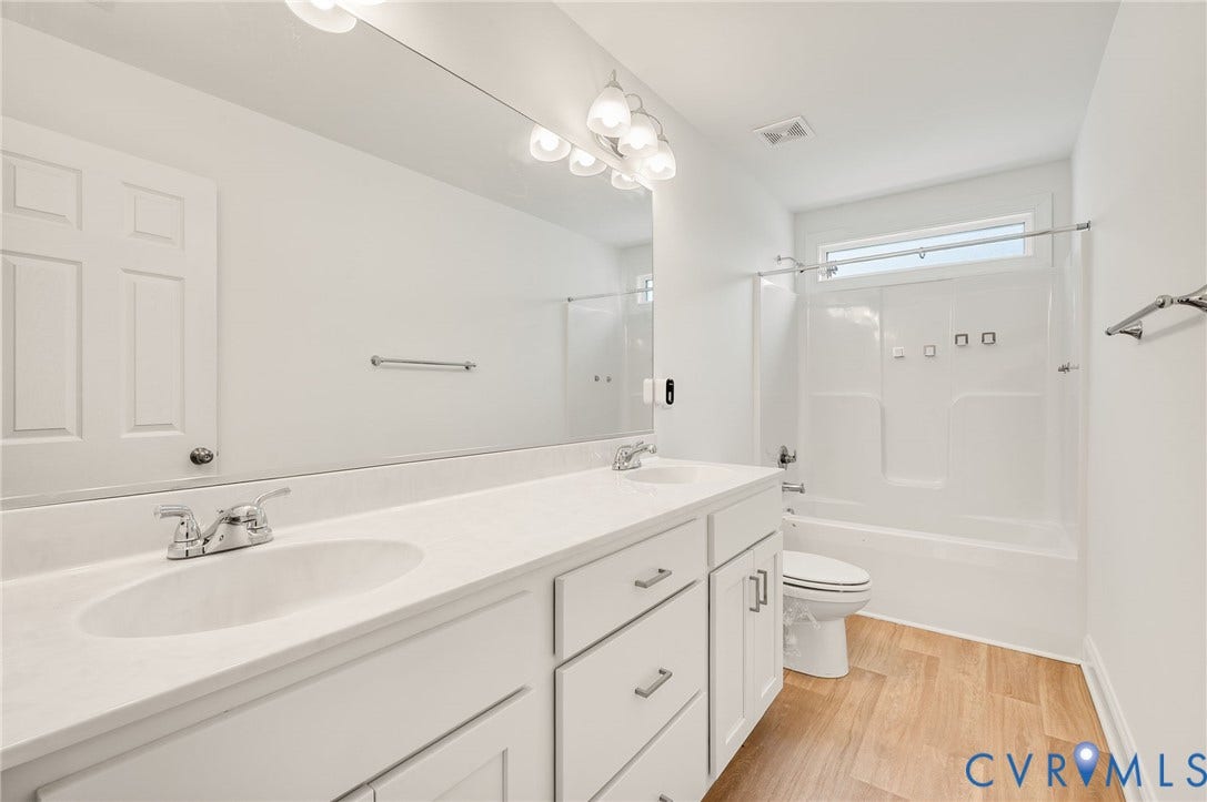 7130 Maple Summit Lane, Moseley, VA 23120 Dual vanity with integrated sinks and chrome fixtures, bright overhead lighting, white cabinetry, a large mirror, and wood-finish flooring