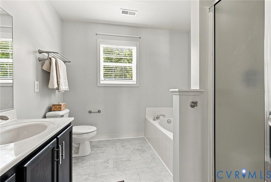 Bathroom featuring a built-in tub, white tiled surround, single vanity with dark cabinetry, and a window with blinds