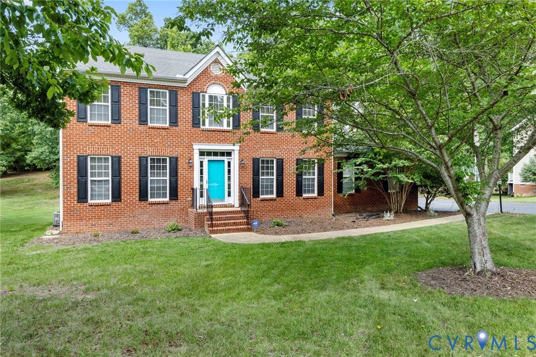Brick two-story colonial-style residence featuring a vibrant blue front door, black window shutters, a front porch with railing, and a mature tree in the foreground