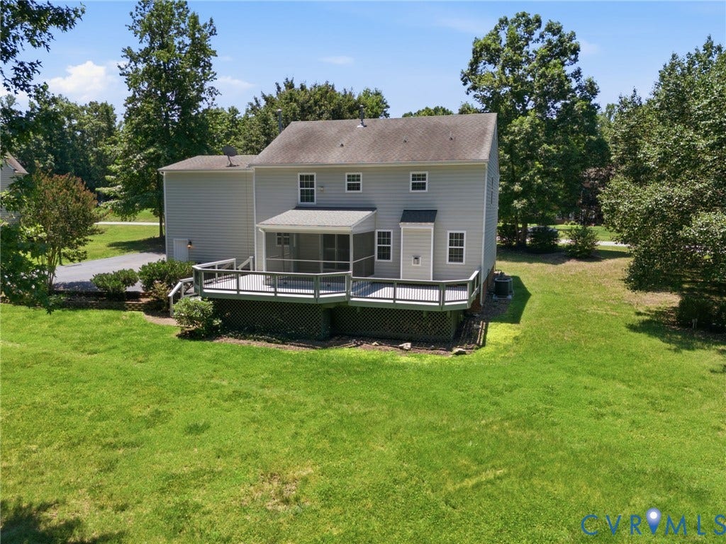 Expansive rear exterior featuring a multi-level deck with screening, ample green space, mature trees, and a gravel driveway