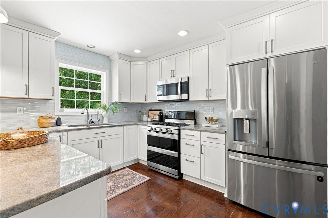 White shaker cabinetry, stainless steel appliances, light-toned stone countertops, a subway tile backsplash, and dark wood-finish flooring