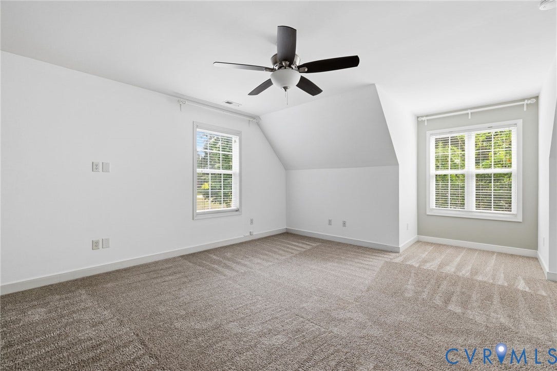 Spacious room featuring vaulted ceilings, a contemporary ceiling fan, and two windows with blinds