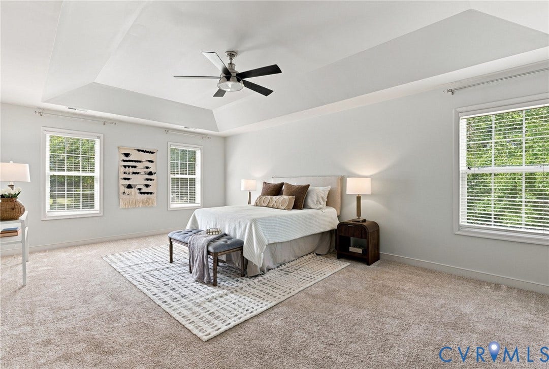 Recessed ceiling with an integrated ceiling fan, multiple double-hung windows, and neutral carpeting