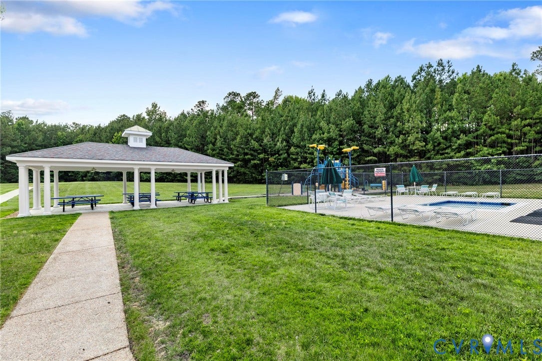 Community amenity area featuring a covered picnic pavilion, swimming pool with surrounding concrete deck, and a fenced recreational water play structure
