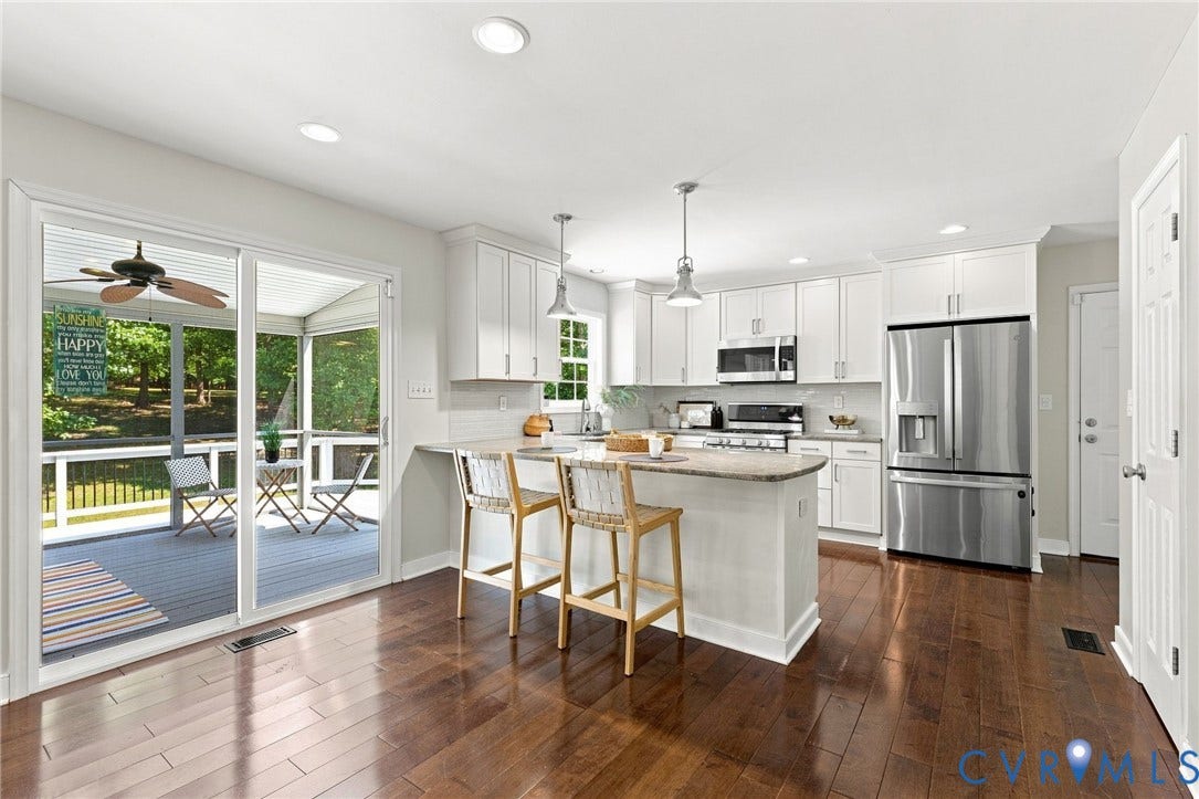 Kitchen featuring wood-finish flooring, white cabinetry, stainless steel appliances, and a central island with counter seating