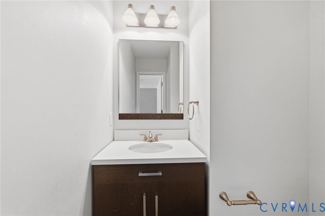 Bathroom vanity featuring a dark wood-finish cabinet, white countertop with an integrated sink, brushed nickel faucet, and a wall-mounted mirror