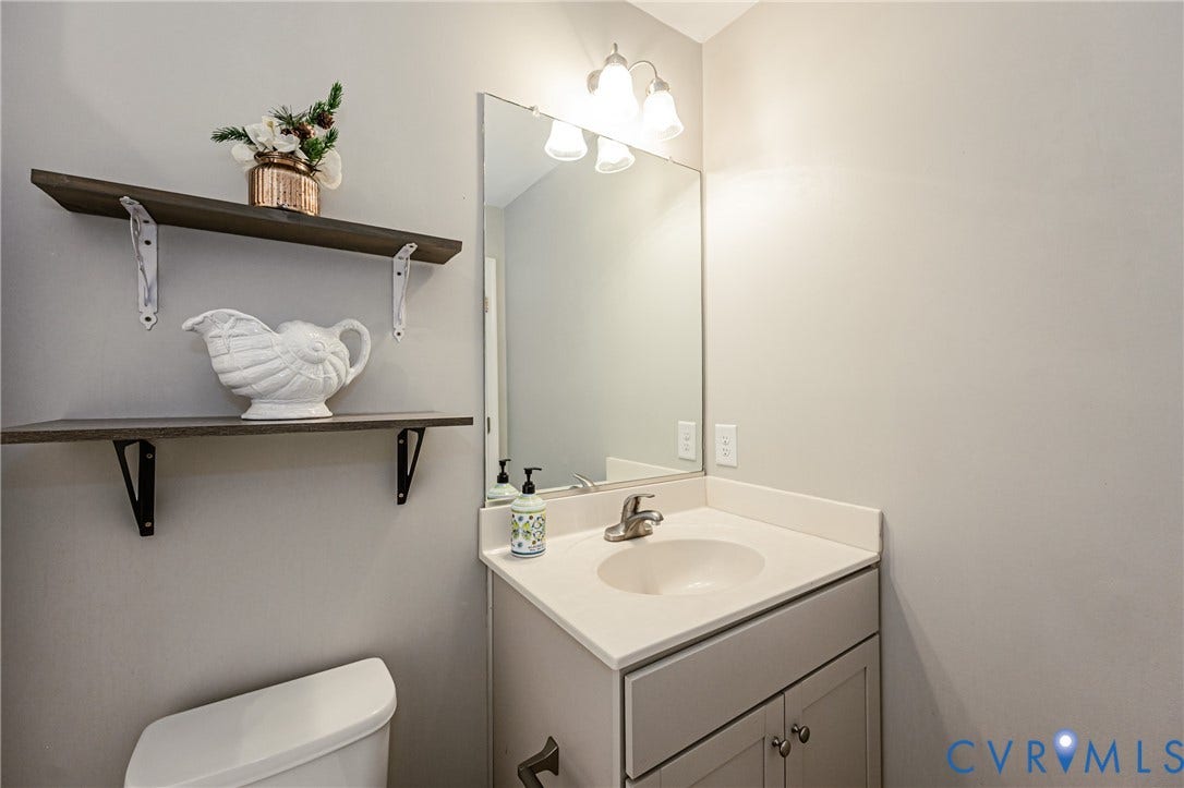 1324 Stone Ridge Park Loop, Henrico, VA 23228 Bathroom vanity featuring a light-toned countertop with integrated sink, brushed nickel faucet, and a mirror with overhead three-bulb light fixture