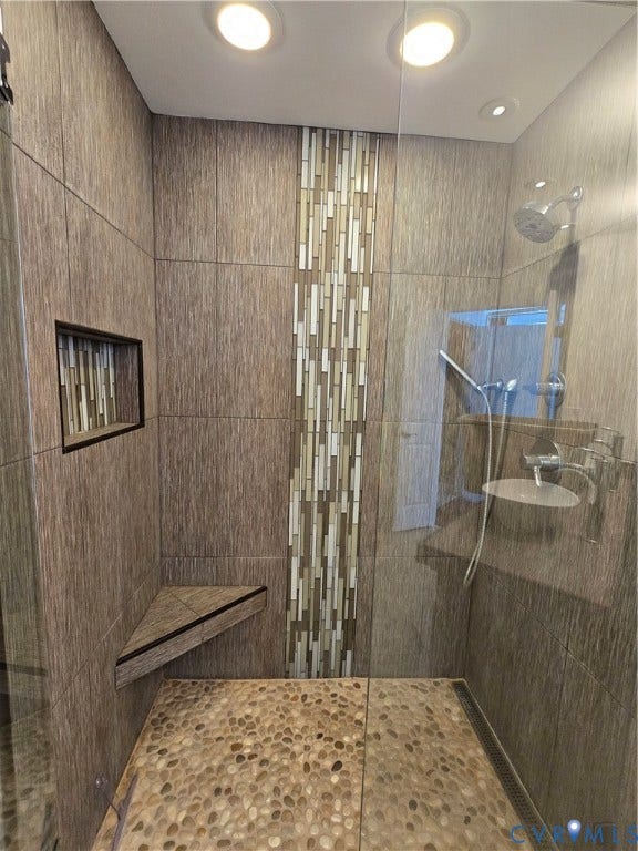1101 Haxall Point, #815, Richmond, VA 23219 Walk-in shower featuring pebble stone flooring, wood-grain tile walls, a decorative vertical tile accent, a built-in corner bench, and a recessed niche