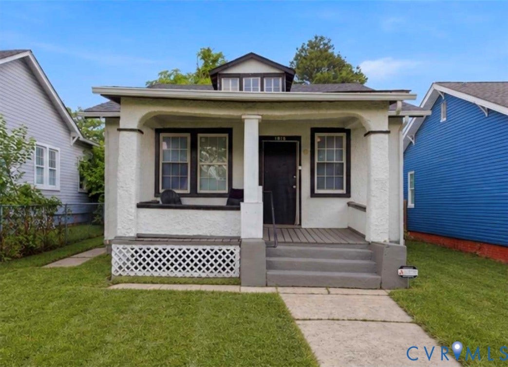 1615 N 19th Street, Richmond, VA 23223 Front exterior featuring a covered porch with a dark wood-finish deck, stucco siding, a black front door, and a dormer window