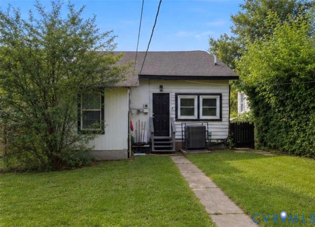 1615 N 19th Street, Richmond, VA 23223 Rear exterior featuring white siding with dark trim, a dark rear entry door, and a concrete pathway through the lawn