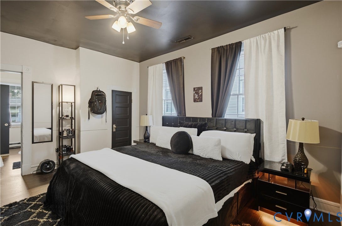 1615 N 19th Street, Richmond, VA 23223 Bedroom featuring a ceiling fan with light kit, two windows with curtain rods, a paneled door, and wood-finish flooring