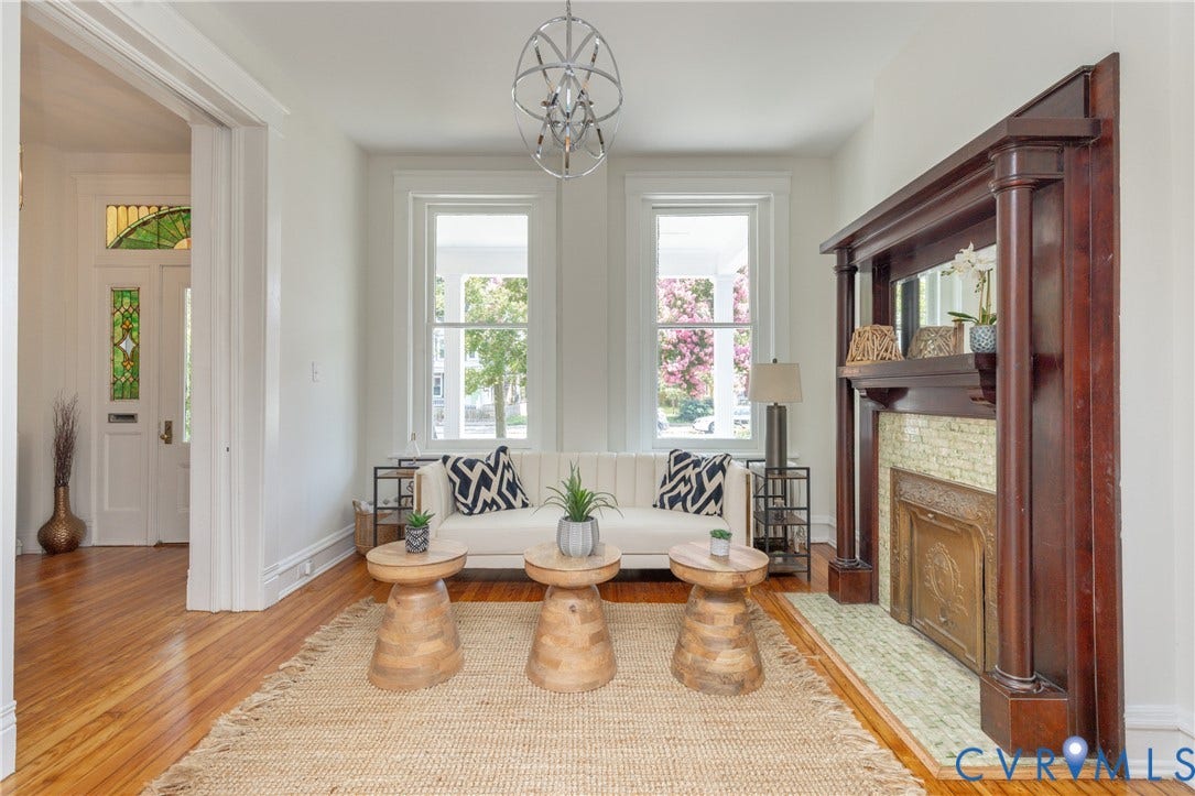 3135 Floyd Avenue, Museum District, Richmond, VA 23221 Living room featuring a prominent dark wood fireplace surround with tiled hearth, natural wood-finish flooring, white walls, and a modern chandelier