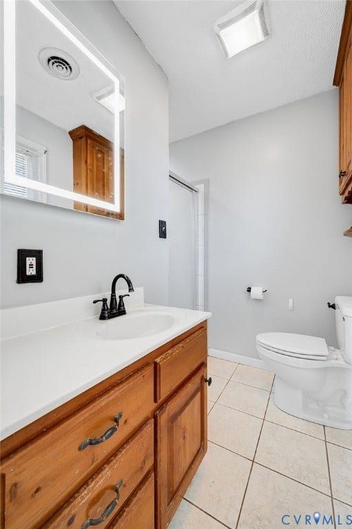 912 Williamsburg Road, Colonial Manor, Colonial Heights, VA 23834 Wood-finish vanity with a white countertop and basin sink, matte black faucet, illuminated mirror, and tiled flooring
