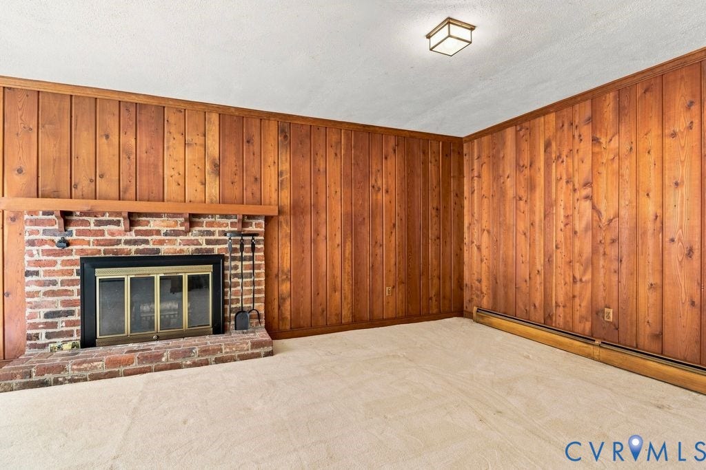 2425 Chancellor Road, North Chesterfield, VA 23235 Brick fireplace with a brass fire screen and wood mantel, complemented by wood-paneled walls and neutral carpeting