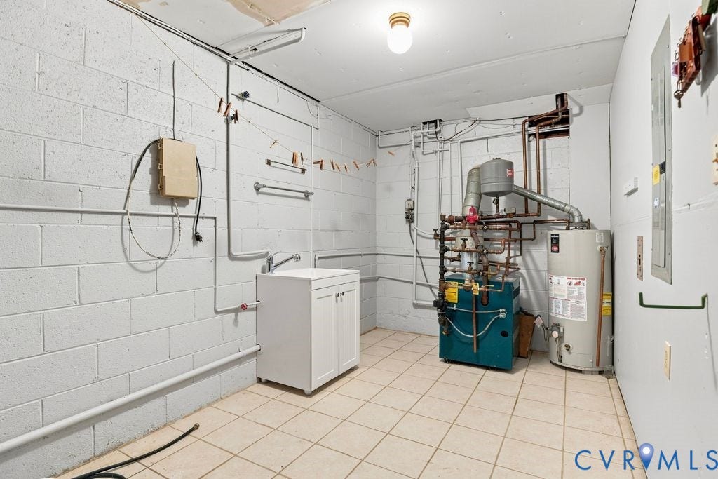 2425 Chancellor Road, North Chesterfield, VA 23235 Utility room with entrance to garage and work area. Tiled flooring and block walls, featuring a utility sink cabinet and exposed piping. Washer and dryer hookup.