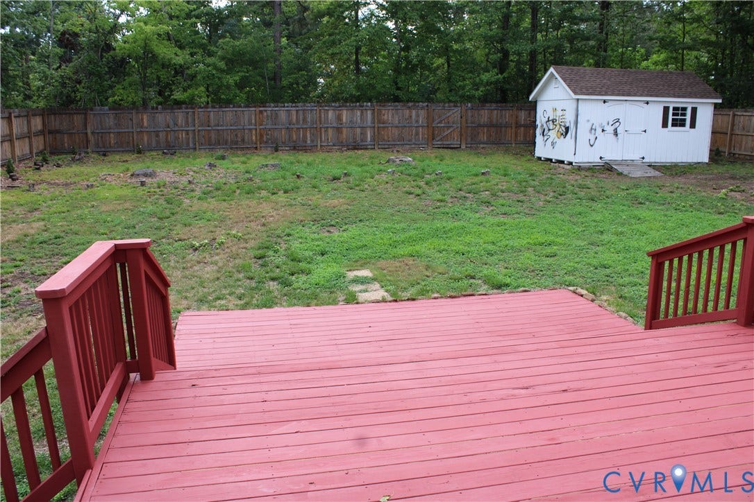 2120 Oakhampton Place, Henrico, VA 23233 Expansive backyard featuring a red-stained wood deck, perimeter wood fencing, a white storage shed with dark shingles, and a partial tree-line border