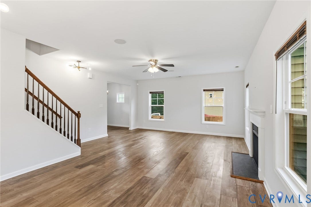 2007 Arcadia Avenue, Chester, VA 23831 Spacious interior featuring wood-finish flooring, a contemporary fireplace with white mantel, a staircase with dark wood handrail and balusters, multiple windows, and a ceiling fan