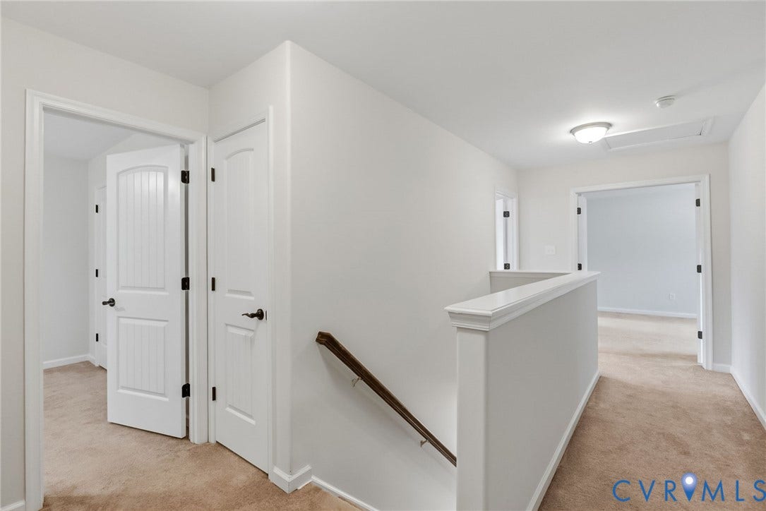 2007 Arcadia Avenue, Chester, VA 23831 Carpeted hallway with white walls and trim, featuring multiple paneled interior doors with black hardware, a stairwell with a wood handrail, and a flush mount ceiling light