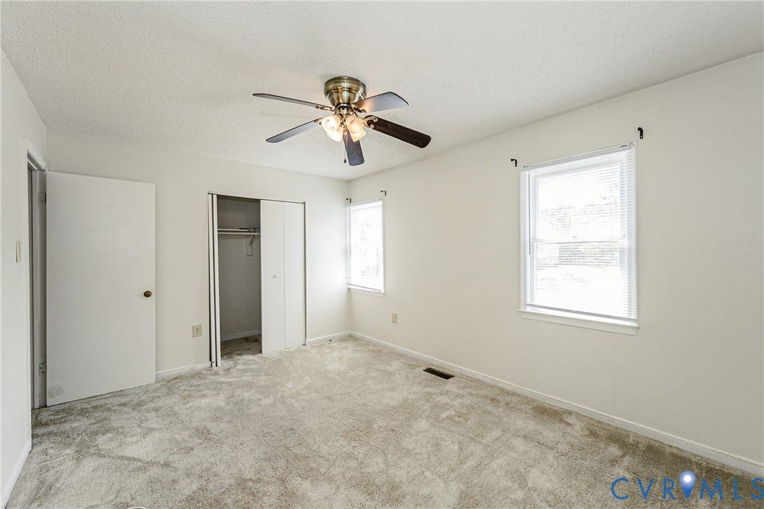 Carpeted interior room featuring a ceiling fan, two windows with blinds, a closet with bi-fold doors, and a door with a round doorknob