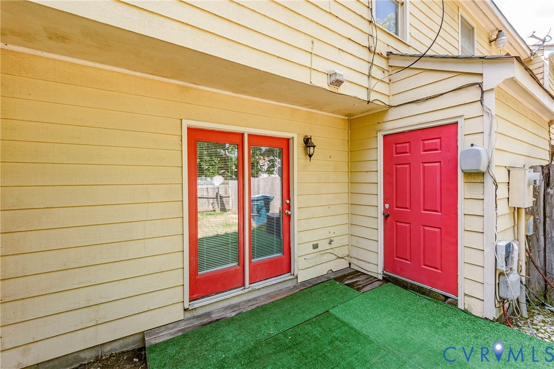 Exterior with horizontal siding, featuring red double doors, a red single door, and a patch of artificial turf