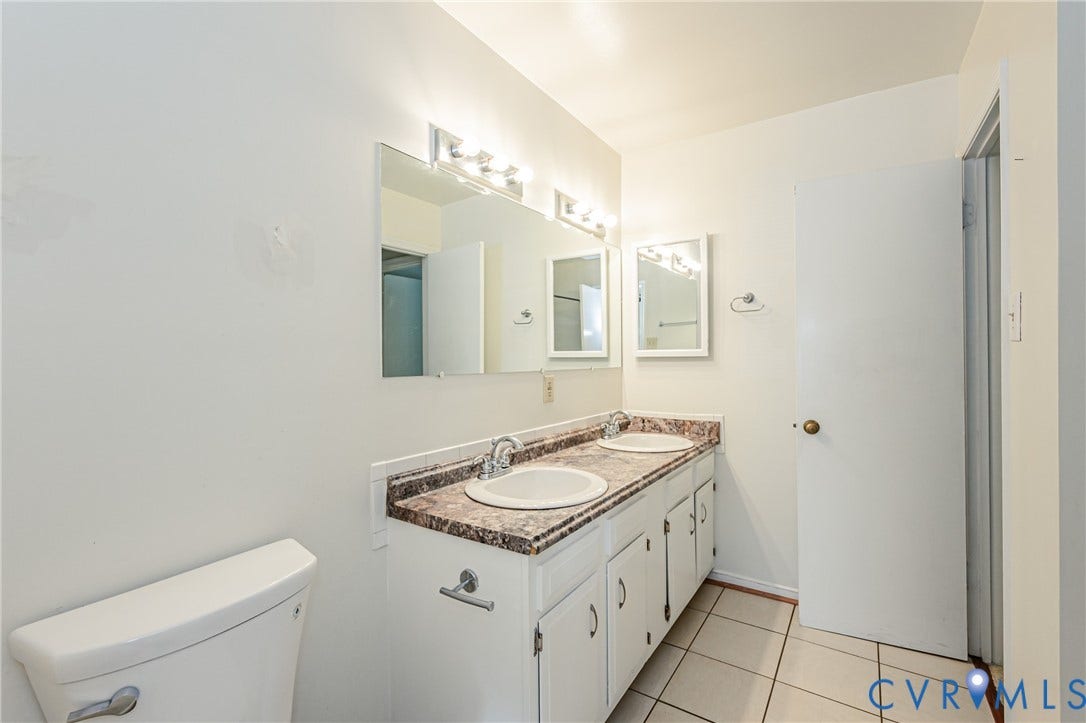 Bathroom featuring a dual vanity with a patterned countertop, two undermount sinks, and white cabinetry