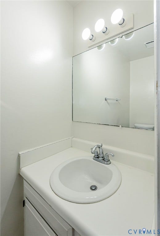 Bathroom vanity featuring a drop-in sink, chrome two-handle faucet, and white laminate countertop with an integrated backsplash