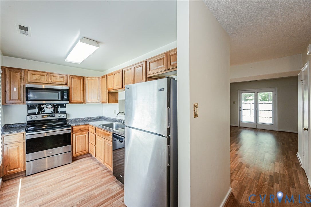 Kitchen featuring wood-finish flooring, stainless steel appliances, wood cabinetry, and granite-style countertops