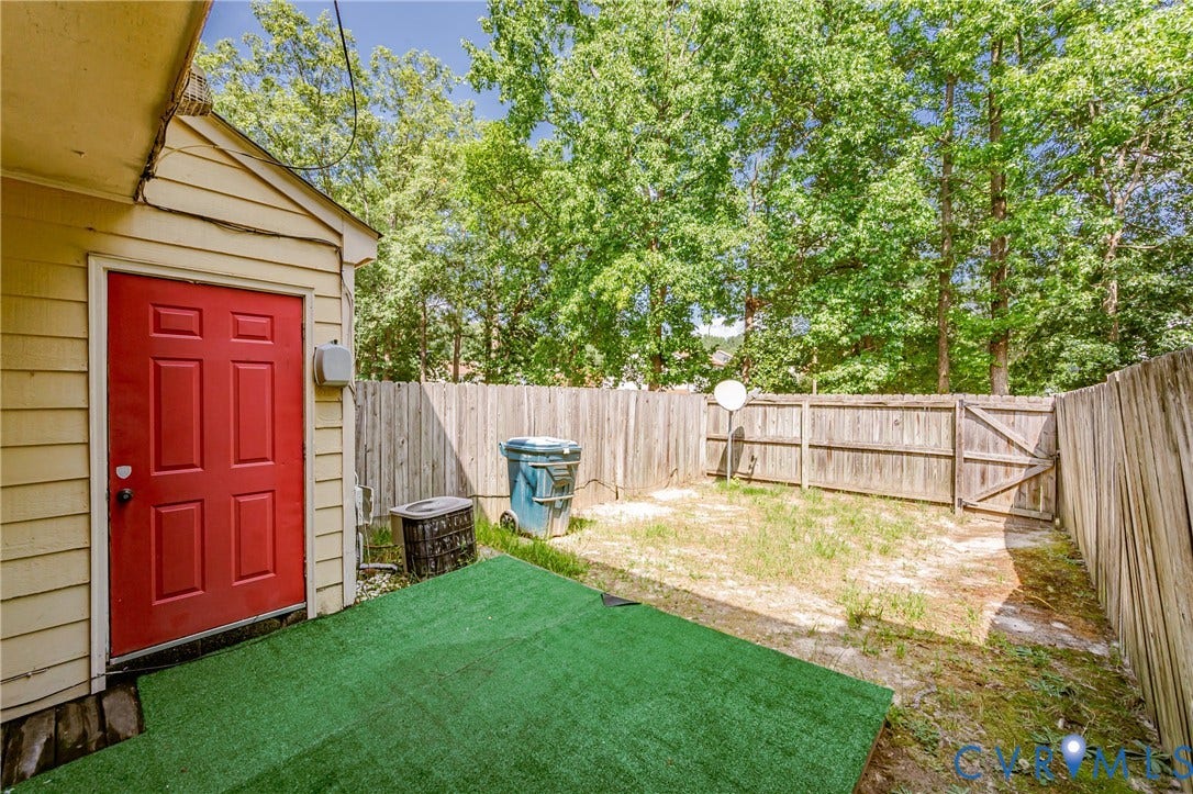 Fenced backyard featuring a red entry door, horizontal siding, and an artificial turf patio area