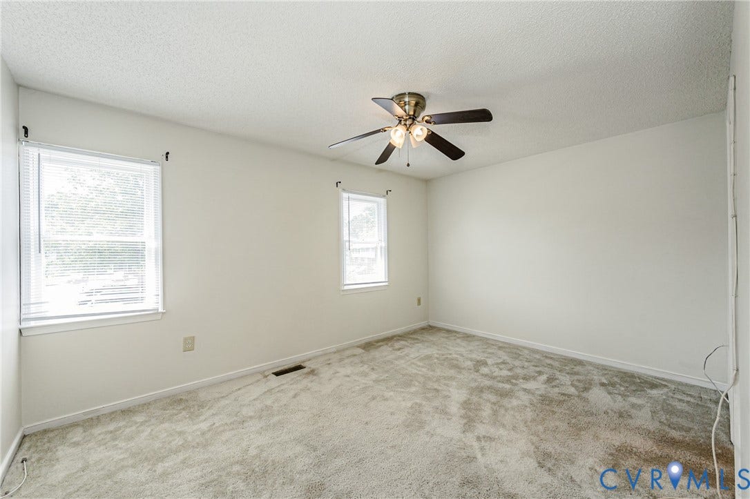 Spacious room featuring light-colored carpeting, white painted walls, and a textured ceiling
