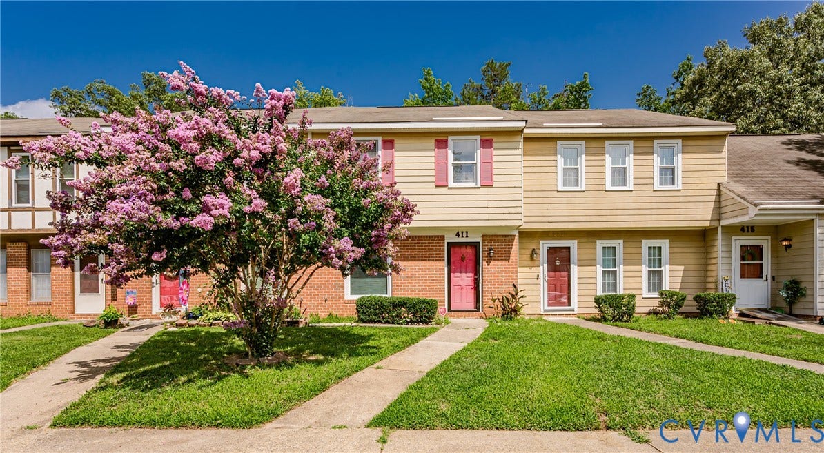 Townhome exterior featuring tan siding, brick accents, and a vibrant flowering tree