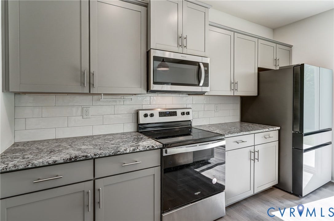 Kitchen featuring gray shaker-style cabinetry with chrome hardware, coordinating stone countertops, and a subway tile backsplash