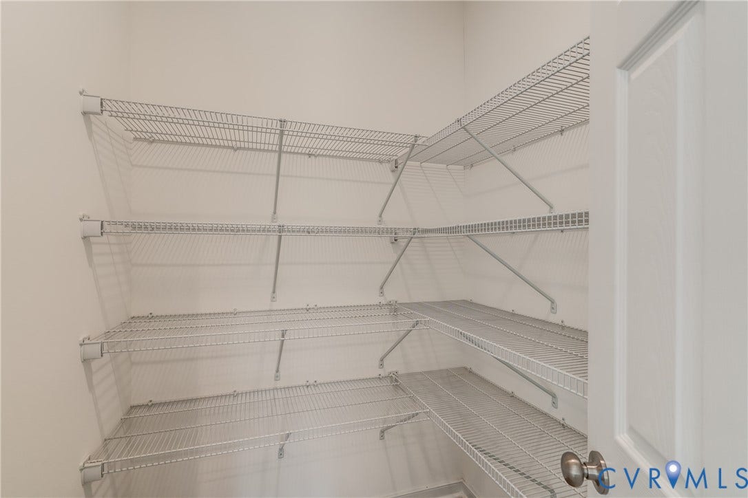 Corner pantry featuring floor-to-ceiling wire shelving, white painted walls, and a paneled door with a brushed nickel knob