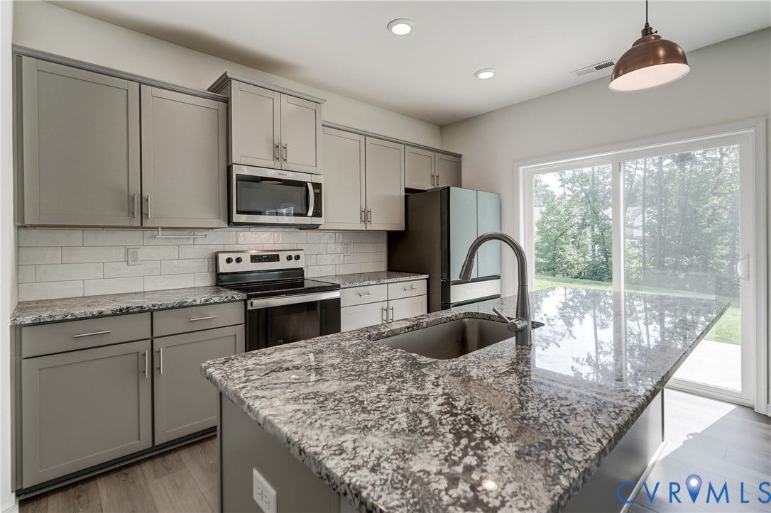 Kitchen featuring an island with an undermount sink, granite countertops, gray cabinetry, stainless steel appliances, and wood-finish flooring