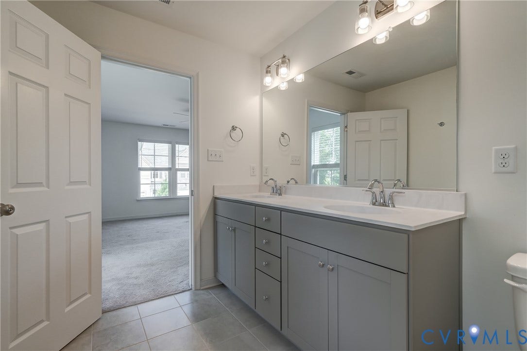 Bathroom featuring a double vanity with grey cabinetry, dual undermount sinks, and a large mirror