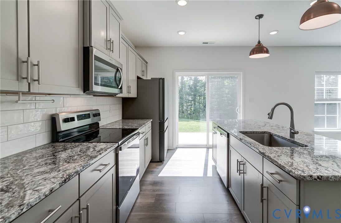Modern kitchen featuring light gray cabinetry, stainless steel appliances, granite countertops, and a subway tile backsplash