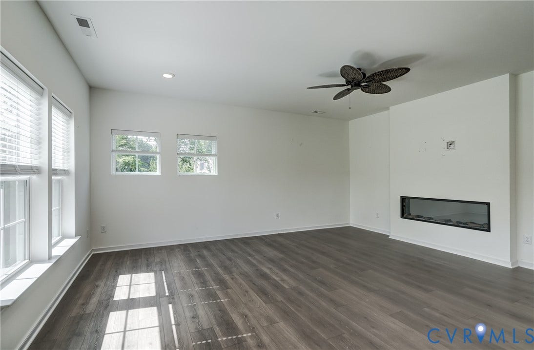 Spacious room featuring wood-finish flooring, multiple windows, a modern linear fireplace, recessed lighting, and a ceiling fan