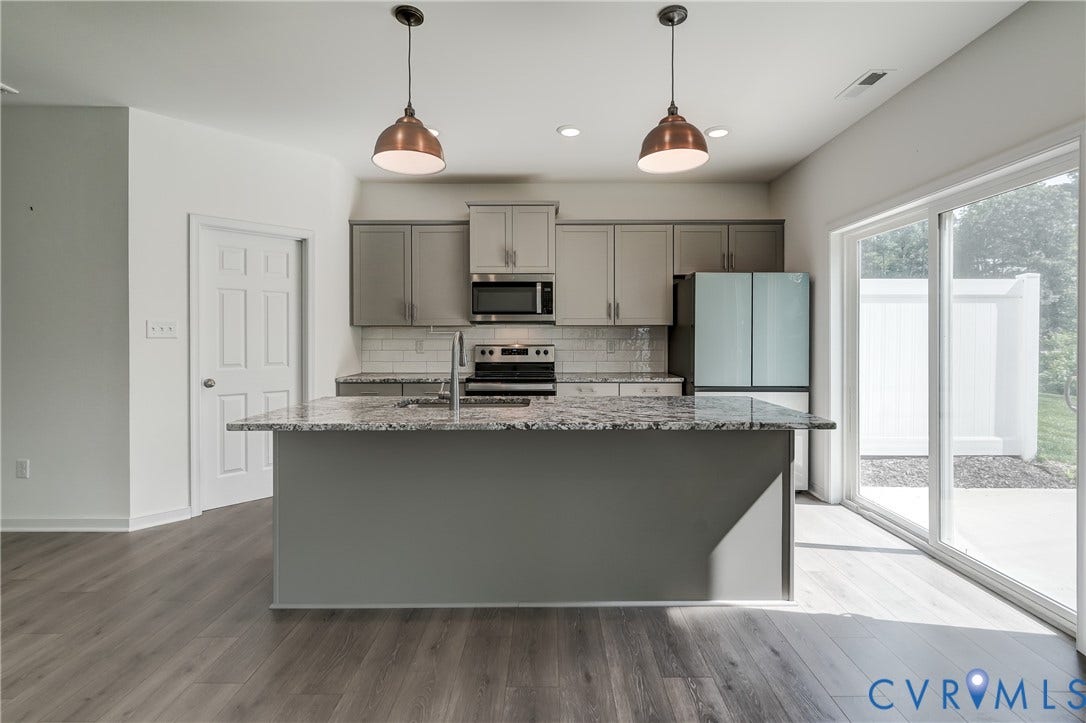 Modern kitchen featuring an expansive center island with integrated sink, granite countertops, wood-finish flooring, two-tone cabinetry, and stainless steel appliances