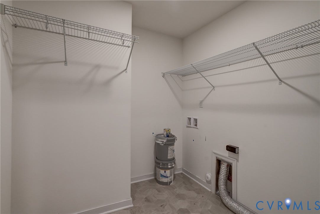 Utility space featuring wire shelving, wall-mounted electrical outlets, and plumbing hookups