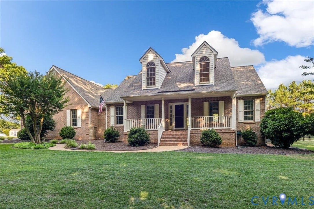 1437 Palmore Road, Powhatan, VA 23139 Traditional brick exterior featuring a covered front porch with white railings, two dormer windows, and a landscaped front yard with a curved path