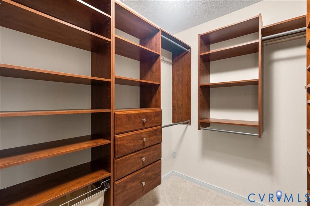 1437 Palmore Road, Powhatan, VA 23139 Custom closet system featuring rich wood-finish shelving, integrated drawers with decorative hardware, multiple hanging rods, and a pull-out hamper