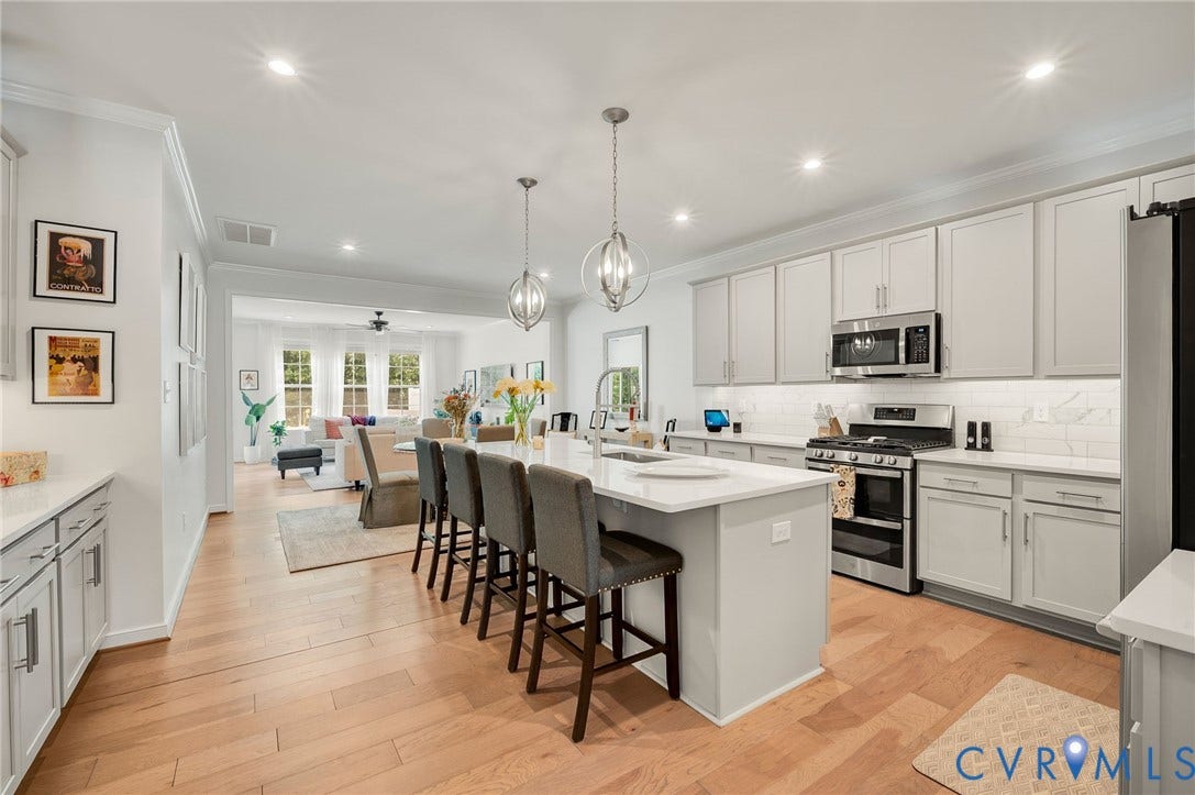 9217 Cerulean Place, Goochland, VA 23238 Kitchen with light wood-finish flooring, featuring a large center island with pendant lighting, light gray cabinetry, stainless steel appliances, and white countertops with a subway tile backsplash